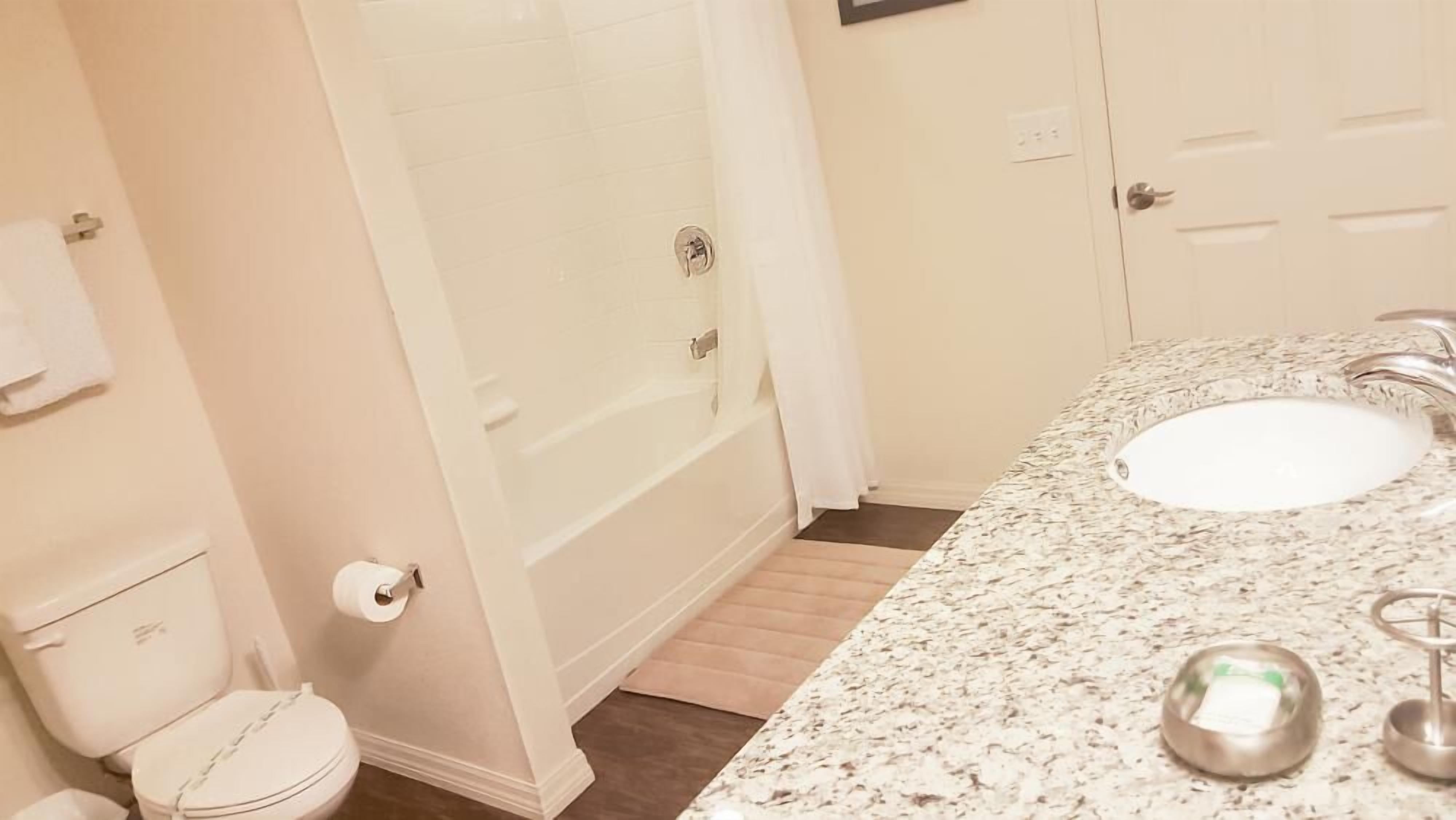 A bathroom with a white toilet, a sink with a marble countertop, and a shower area.