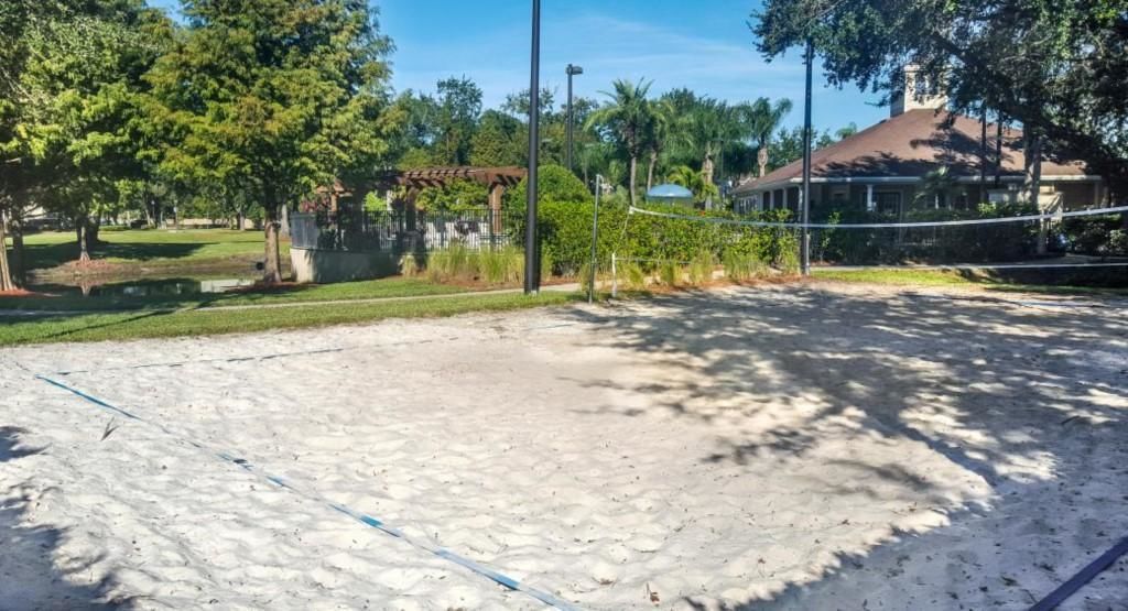 Una cancha de voleibol de arena con árboles y una casa al fondo.