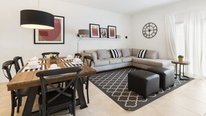 A modern living room with a dining area, a sofa set, a coffee table, and a black ottoman. - Villa Rodrigues - Encantada Resort (Kissimmee)