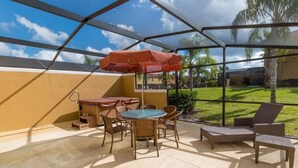 A covered patio area with a table and chairs, a barbecue grill, and a red umbrella. - Villa Rodrigues - Encantada Resort (Kissimmee)