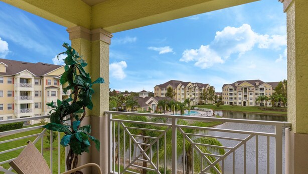 A balcony with a view of a lake, surrounded by greenery and buildings.