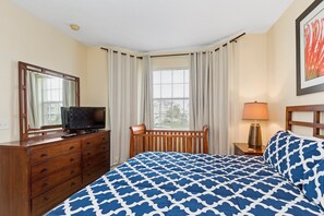 Een hotelkamer met een bed, een houten dressoir, een televisie, een lamp en een raam met gordijnen.