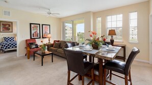 A spacious living room with a dining area, featuring a large window, a ceiling fan, and a cozy seating arrangement.
