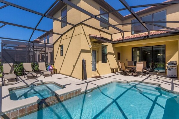 A pool area with a glass-enclosed structure, lounge chairs, and a patio with a table and chairs.