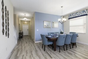 A dining area with a table set for four, a chandelier, and a window with blinds.