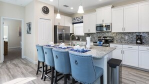 Una cocina moderna con armarios blancos, encimera de granito, electrodomésticos de acero inoxidable y taburetes de bar azules.