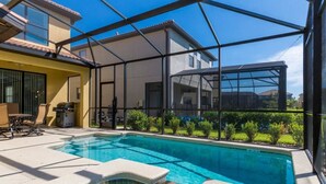 Una piscina con cerramiento de vidrio, un patio con mobiliario exterior y vista a un edificio residencial al fondo.