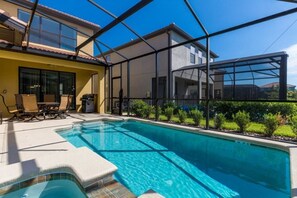 A swimming pool with a glass enclosure, a patio area with chairs, and a view of a house.
