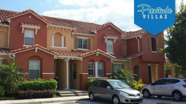 Une rangée de villas rouges aux toits de tuiles, une voiture garée devant, et une enseigne indiquant « Plentitude Villas ».