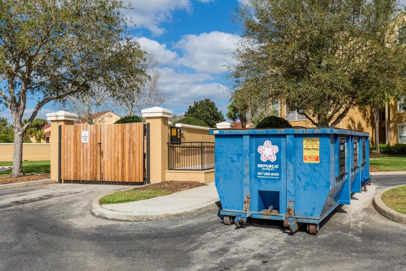 A blue dumpster with a recycling logo and a caution sign, parked on a residential street.