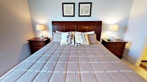 A neatly made bed with a patterned bedspread and two pillows, flanked by nightstands with lamps. - Villa Nogueira - West Lucaya (Kissimmee)
