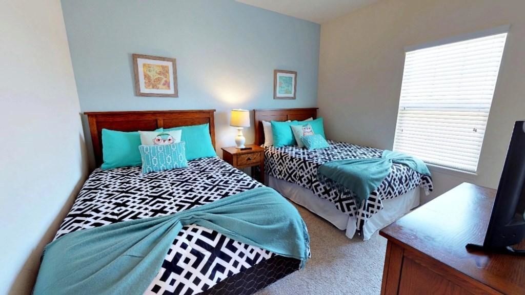 Une chambre avec deux lits, chacun agrémenté de draps à motifs, une table de chevet avec une lampe et un téléviseur posé sur un meuble en bois.