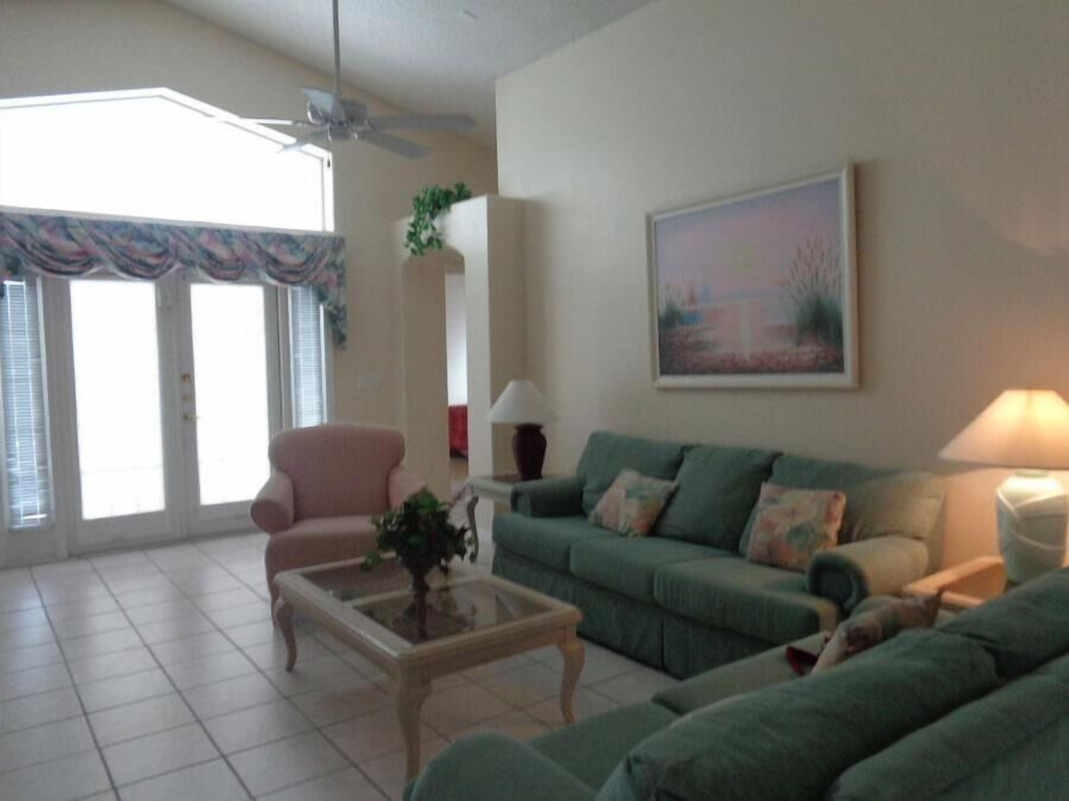A living room with a green sofa, a pink armchair, a glass coffee table, and a painting on the wall.