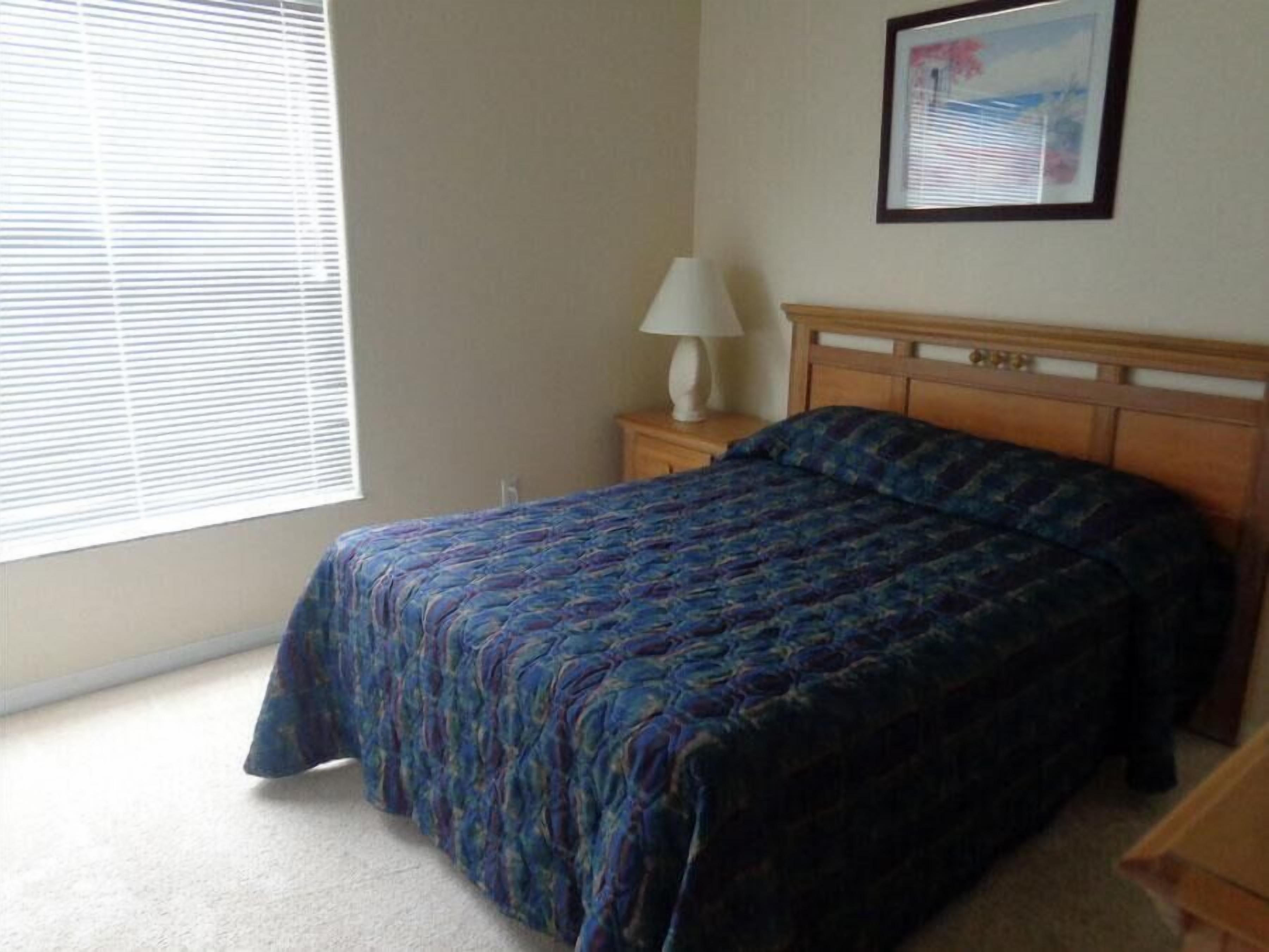 A bedroom with a bed, a nightstand, a lamp, and a window with blinds.