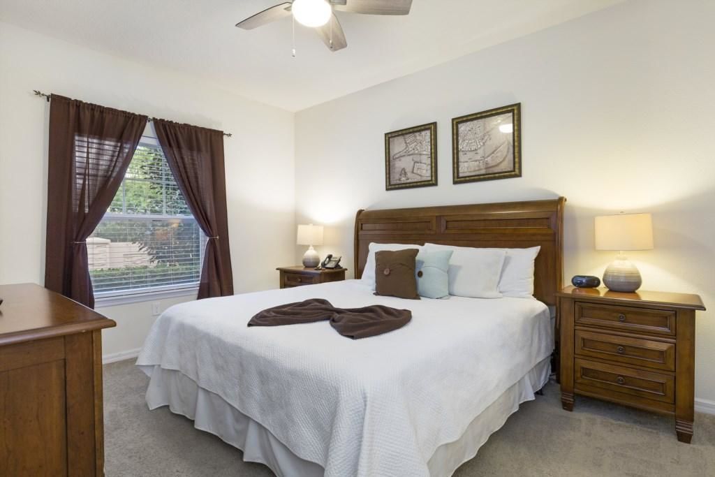 A neatly arranged bedroom with a large bed, two bedside tables with lamps, a wooden nightstand, and a ceiling fan.