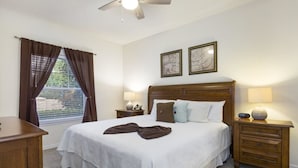 A neatly arranged bedroom with a large bed, two bedside tables with lamps, a wooden nightstand, and a ceiling fan. - Villa CVX- Lucaya Village (Kissimmee)