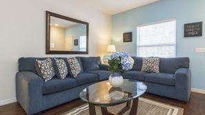 A living room with a blue sofa, a glass coffee table, a mirror, and two motivational wall signs. - Villa CVX- Lucaya Village (Kissimmee)