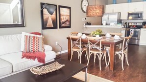 A modern living room with a sofa, dining table, and chairs. There is a kitchen area with appliances and a hanging light fixture. - Villa Guadalupe - West Lucaya (Kissimmee)