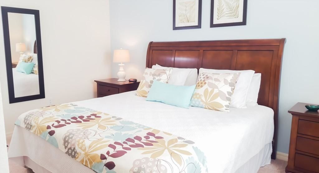 A neatly made bed with a floral bedspread, a wooden headboard, bedside lamps, and a small nightstand with a lamp.