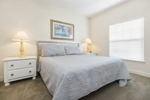 A bedroom with a bed, two bedside tables with lamps, a framed picture on the wall, and a window with blinds.