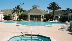 A swimming pool area with lounge chairs and palm trees, surrounded by buildings with a central gazebo-like structure. - Villa Encantada - Windsor Palms (Kissimmee)
