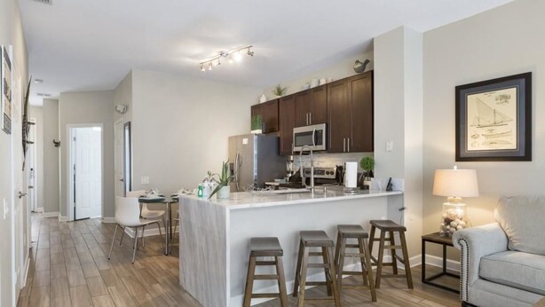 A modern kitchen with a central island, bar stools, and a dining area with chairs. - Villa Encantada - Windsor Palms (Kissimmee)