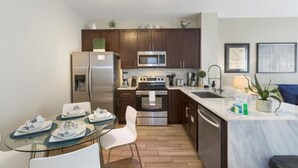 A modern kitchen with stainless steel appliances, a glass dining table, and a small island with a sink. - Villa Encantada - Windsor Palms (Kissimmee)