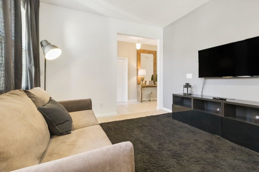 A living room with a sofa, a flat-screen TV mounted on the wall, and a dark rug.