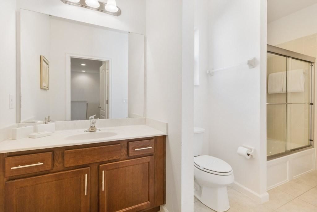 A bathroom with a wooden vanity, a large mirror, a toilet, and a glass shower enclosure.