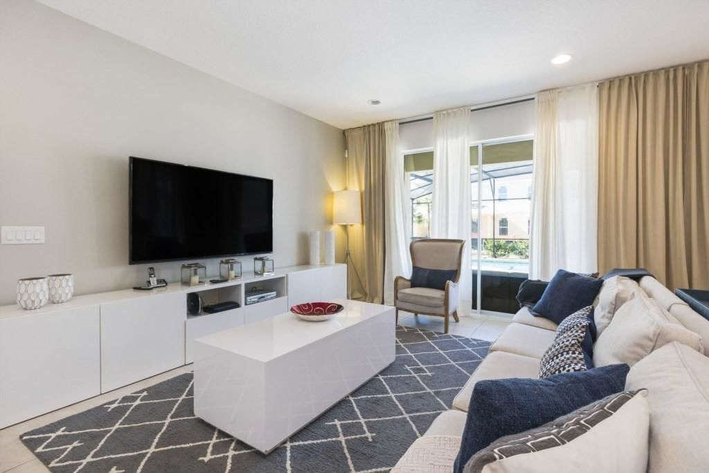 A modern living room with a flat-screen TV, a white coffee table, a sofa, and a chair.