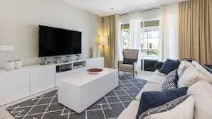 Ein modernes Wohnzimmer mit Flachbildfernseher, weißem Couchtisch, Sofa und Sessel.