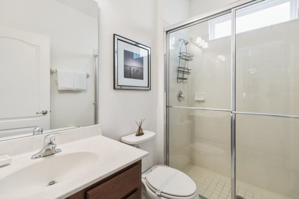 A modern bathroom with a white sink, vanity, toilet, and a glass shower enclosure.