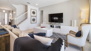 Ein modernes Wohnzimmer mit Sofa, Sessel und Fernseher.