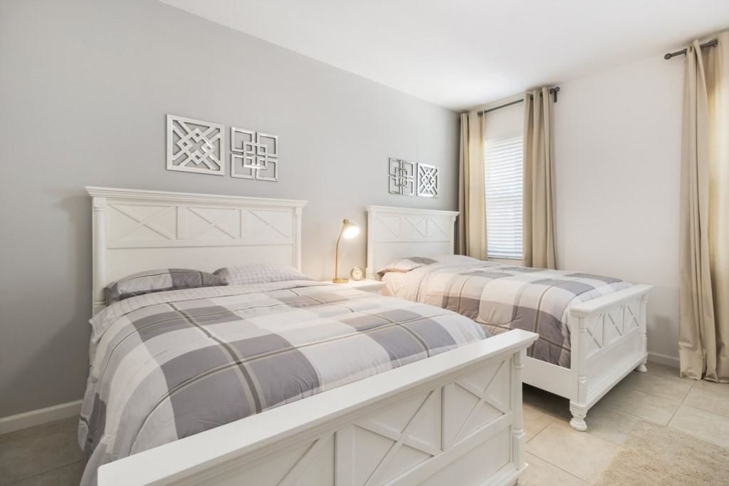 Une chambre avec deux lits, une tête de lit blanche, une table de chevet avec une lampe et des œuvres d’art décoratives au mur.
