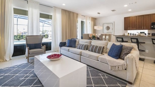 Ein modernes Wohnzimmer mit Sofa, Sesseln und Couchtisch. Es gibt eine Küchenzeile mit Schränken und einer Mikrowelle.