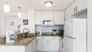 A compact kitchen with white cabinets, a granite countertop, a built-in microwave, a refrigerator, and a coffee maker. - Villa Yamagi - The Enclave Hotel & Suites (Orlando)