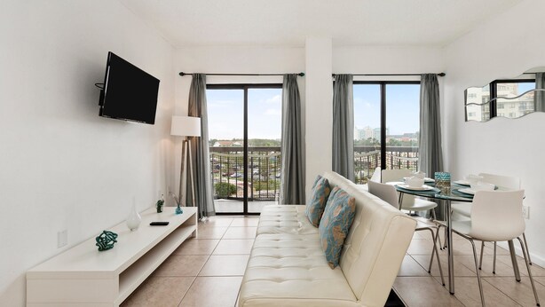 A modern living room with a sofa, a glass dining table, and a TV mounted on the wall. - Villa Yamagi - The Enclave Hotel & Suites (Orlando)