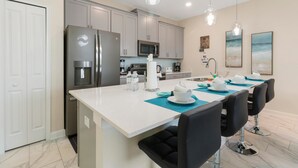 A modern kitchen with grey cabinets, stainless steel appliances, and a central island with black chairs.