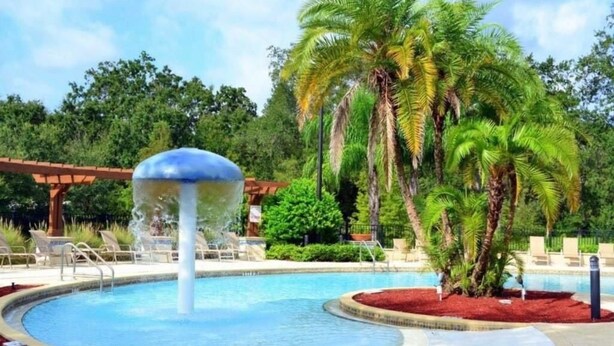 Piscina com uma fonte, rodeada por palmeiras e espreguiçadeiras.