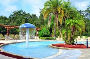 Una piscina con fuente de agua, rodeada de palmeras y sillas de descanso.