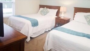 Ein Hotelzimmer mit zwei Betten, jeweils mit einem Holz-Kopfteil, einem Nachttisch mit Lampe und einem Fernseher auf einem Holzgestell.