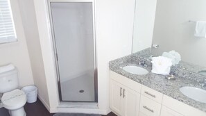 Un baño con ducha de vidrio, dos lavamanos, un espejo grande y un inodoro.