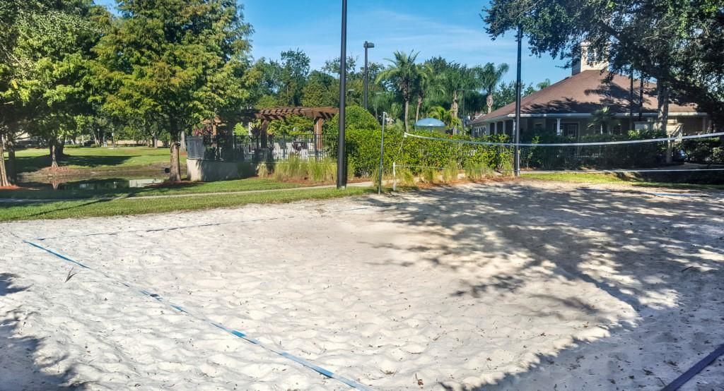 A sandy volleyball court with trees and a house in the background.