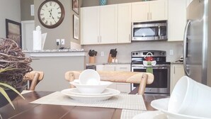A modern kitchen with light-colored cabinets, stainless steel appliances, and a dining area with a wooden table and chairs. - Villa Aventura - Lucaya Village (Kissimmee)
