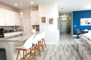 A modern kitchen with white cabinets, a granite countertop, and a central island with bar stools. - Villa Sweet - Storey Lake (Kissimmee)