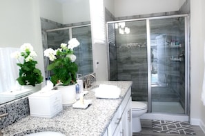A modern bathroom with a granite countertop, white fixtures, and a glass-enclosed shower. - Villa Sweet - Storey Lake (Kissimmee)