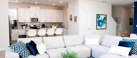 A modern living room with a sectional sofa, a coffee table, and a kitchen in the background.