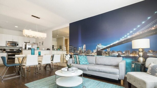 Een moderne woonkamer met uitzicht op een stadsbeeld, een eetgedeelte met witte meubels, en een keuken met roestvrijstalen apparatuur.