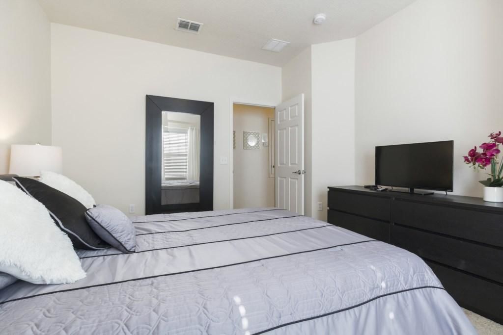 A bedroom with a bed, a TV on a dresser, and a door leading to another room.