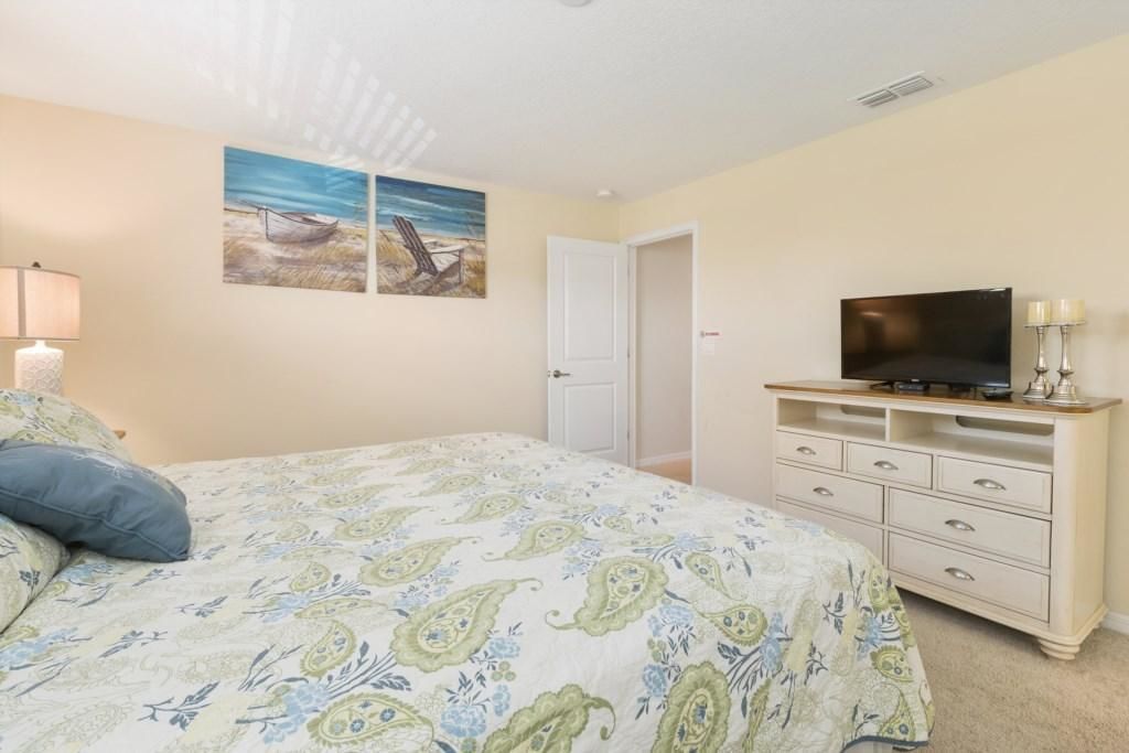 A bedroom with a bed, a TV on a dresser, and two paintings on the wall.
